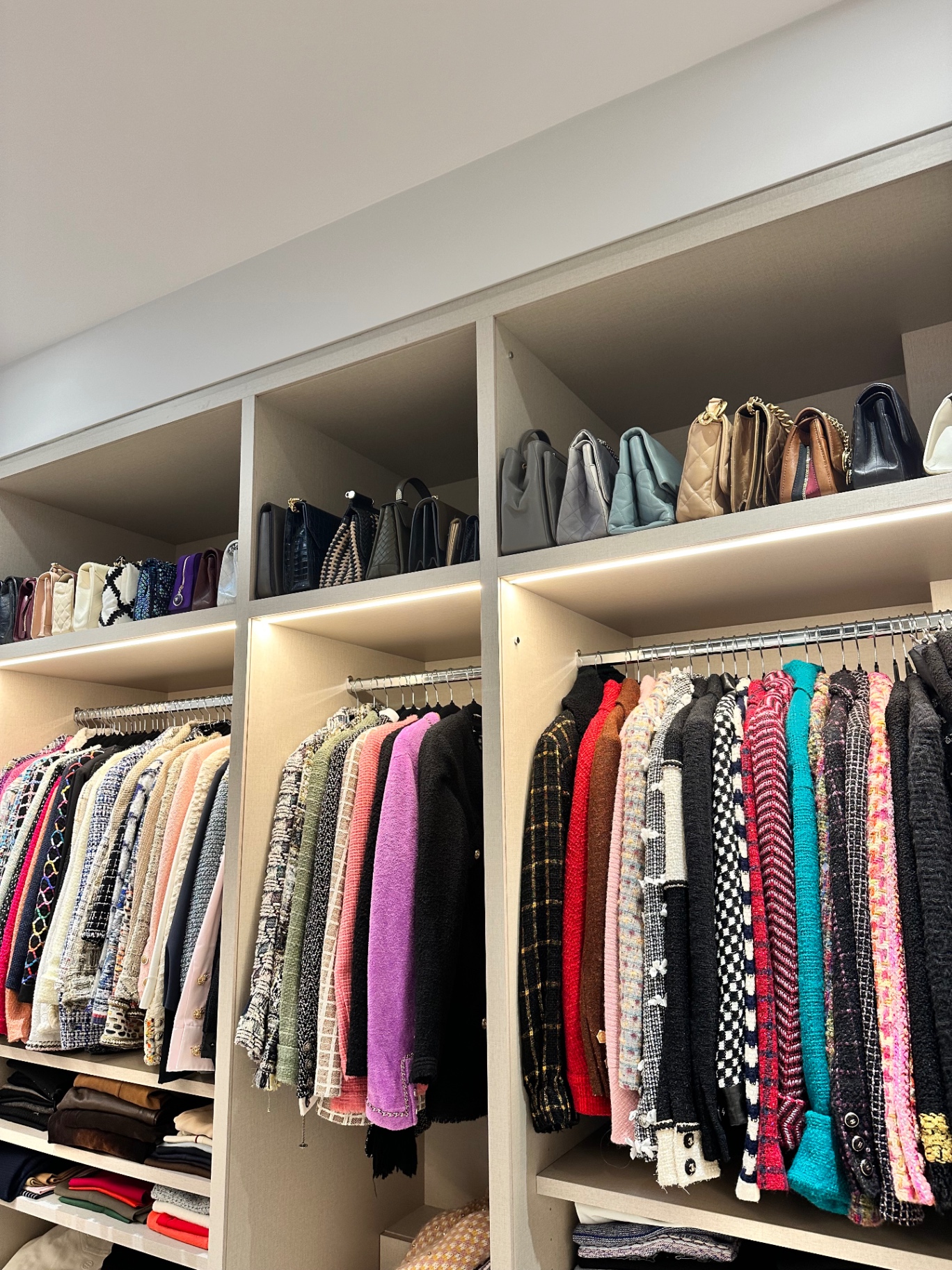 Chanel tweed jackets on rails beneath handbag shelves
